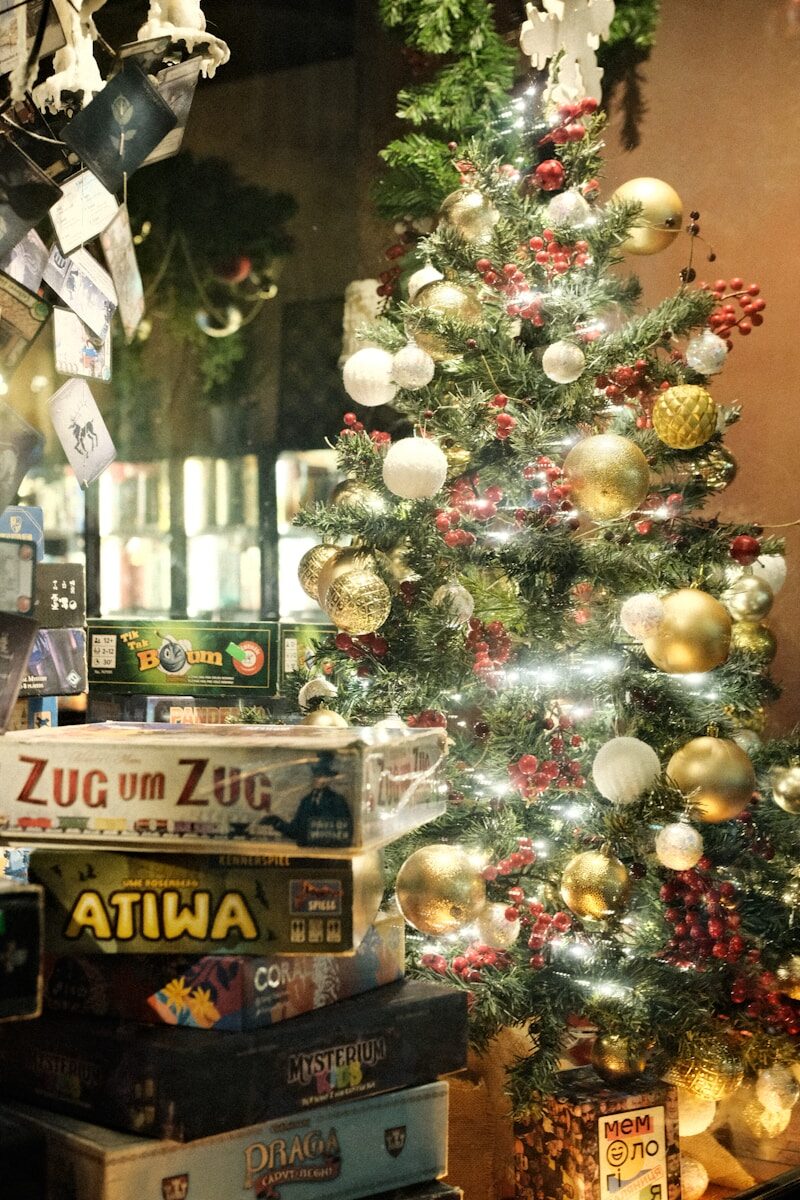 Board games stacked beside a decorated christmas tree.